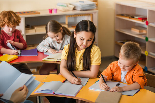 multiethnic kids writing in notebooks during lesson in montessor