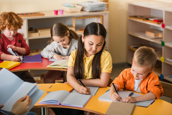 multiethnic kids writing in notebooks during lesson in montessor