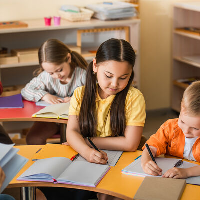 multiethnic kids writing in notebooks during lesson in montessor