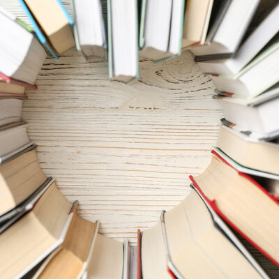 Heart made of books on white wooden rustic background, top view