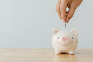 Concept of save money financial business investment. Hand of a man putting coins in piggy bank on wood table