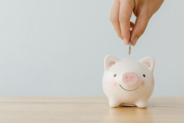 Concept of save money financial business investment. Hand of a man putting coins in piggy bank on wood table