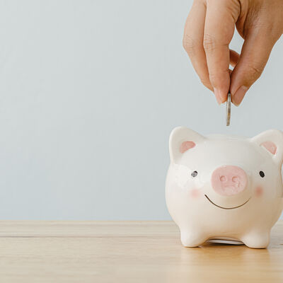 Concept of save money financial business investment. Hand of a man putting coins in piggy bank on wood table