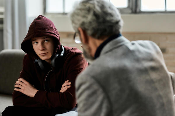 Psychotherapist talking to troubled teenage boy in hood