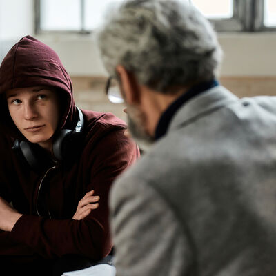 Psychotherapist talking to troubled teenage boy in hood