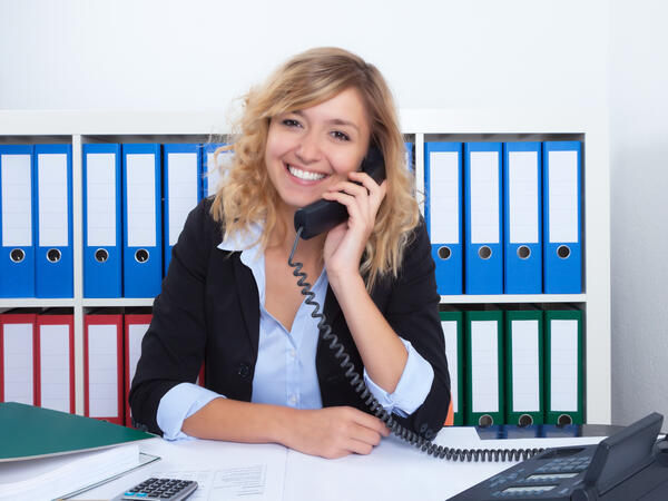 Frau mit blonden Locken im Büro lacht am Telefon
